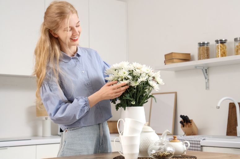 Linda jovem mulher feliz com buquê de flores de crisântemo branco na cozinha em casa