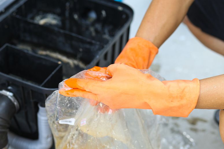 Mulher utilizando luvas e saco de lixo para limpar a caixa de gordura