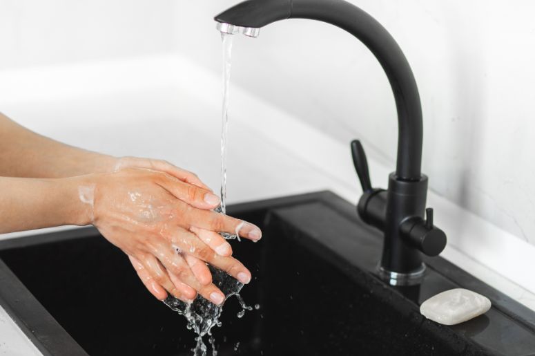 mulher lavando as mãos em uma torneira preta