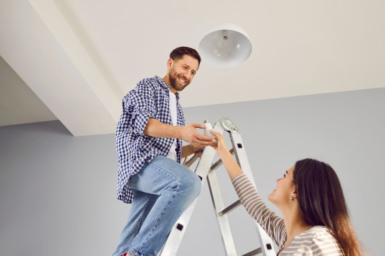 Casal instalando l&acirc;mpada em casa