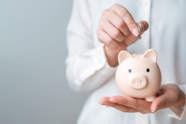 Close de uma pessoa colocando uma moeda em um porquinho