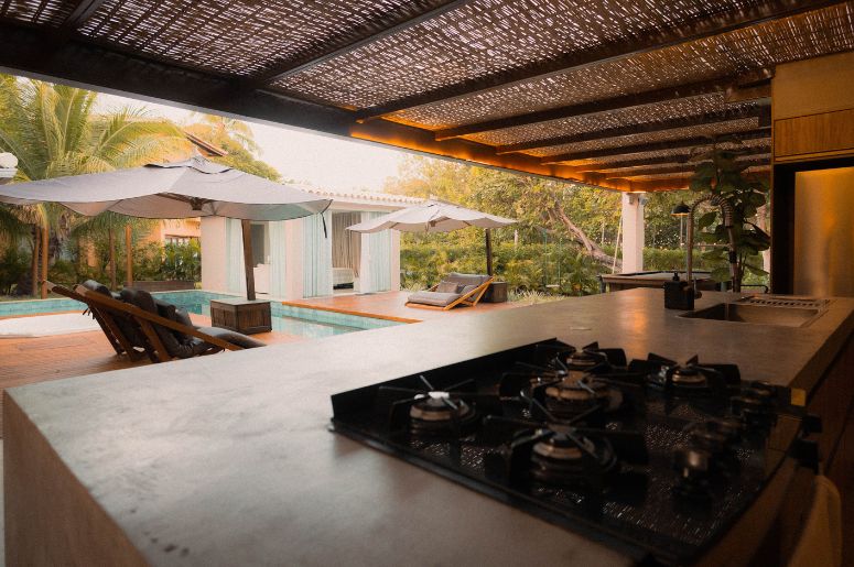 Varanda gourmet com cozinha integrada, bancada, cooktop, piscina e área de lazer ao ar livre