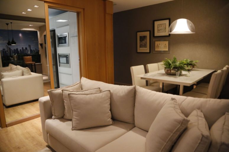 Ambientes integrados com sala de estar, sofá claro, sala de jantar com mesa retangular, cozinha ao fundo e decoração em tons neutros