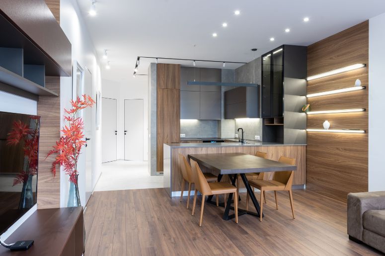 Ambientes integrados com sala de estar, cozinha planejada, mesa de jantar, painel de madeira iluminado e decoração moderna em conceito aberto