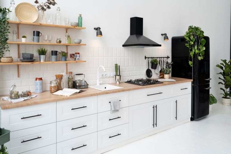 Cozinha branca com bancada de madeira, prateleiras abertas, eletrodomésticos pretos e plantas decorativas