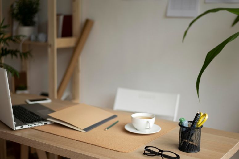 Escritório em casa com escrivaninha de madeira, notebook, cadernos, xícara, porta-canetas e plantas ao redor