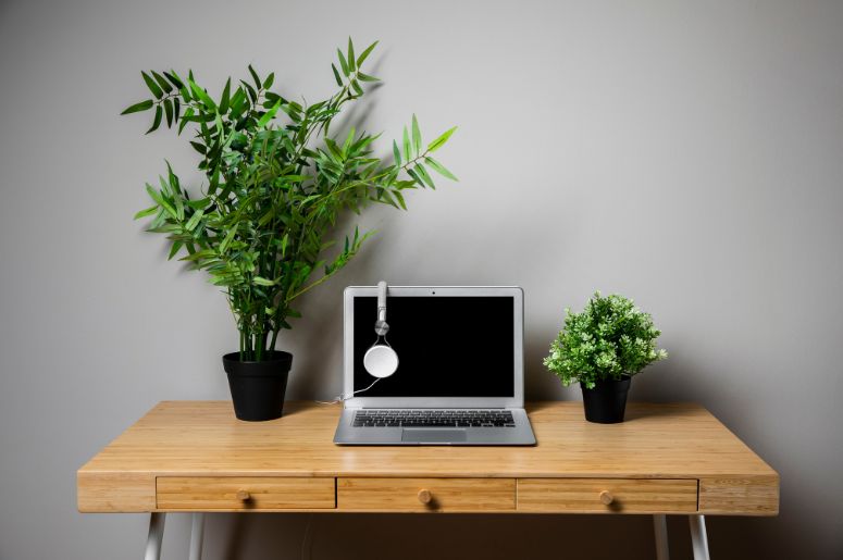 Escrivaninha de madeira com gavetas, notebook, fones de ouvido e vasos de plantas sobre a mesa