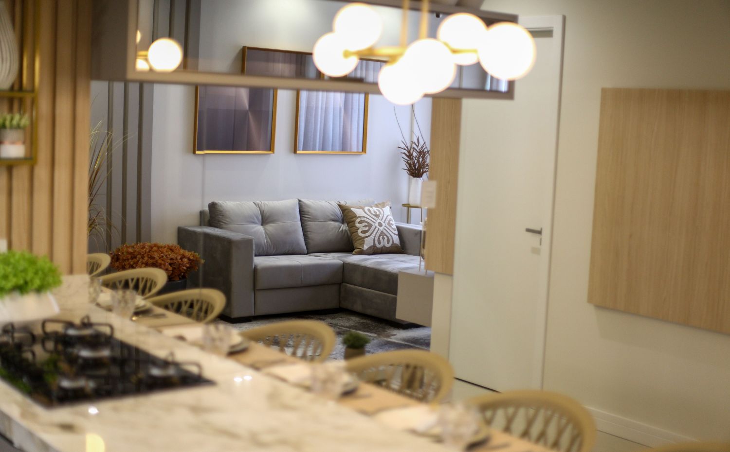 Cozinha com bancada e banquetas integrada à sala de estar com sofá de canto cinza e decoração moderna