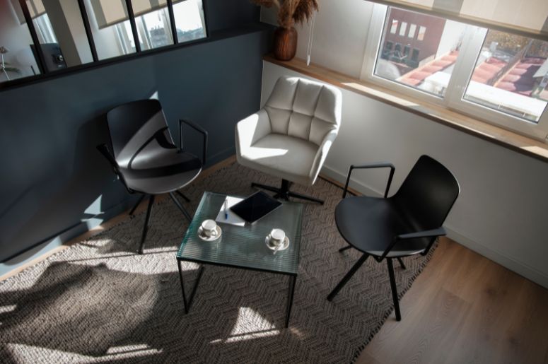 Três modelos de cadeiras modernas com braços, incluindo duas cadeiras pretas e uma poltrona estofada branca, compondo um ambiente contemporâneo para reuniões ou convivência