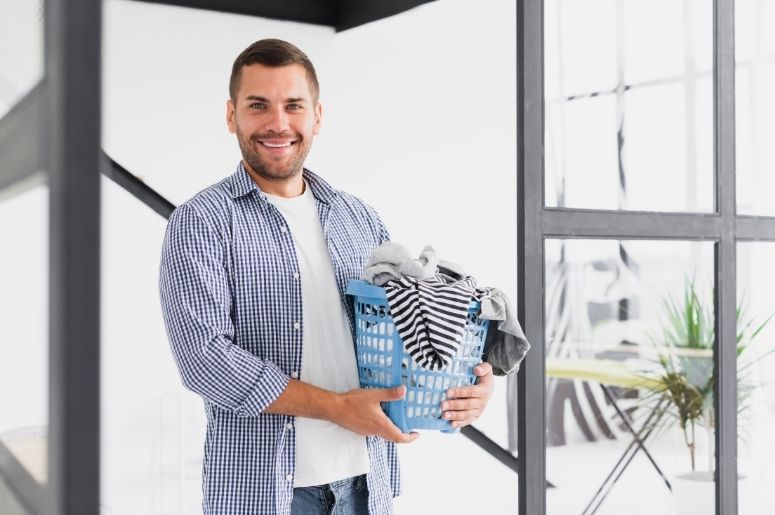 Homem segurando cesto azul com roupas em ambiente claro e moderno