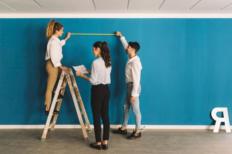 Pessoas medindo uma parede azul com fita métrica