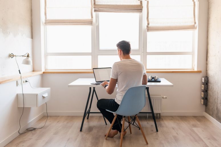 Home office compacto com escrivaninha, cadeira e notebook posicionados próximos à janela