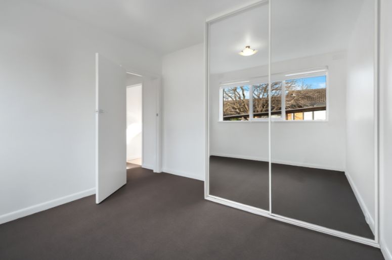 Quarto branco com armário planejado de portas de correr espelhadas, janela ampla, piso escuro e paredes claras