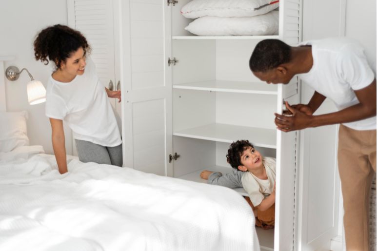 Casal organizando roupas em um armário planejado branco no quarto, enquanto uma criança aparece brincando dentro do móvel
