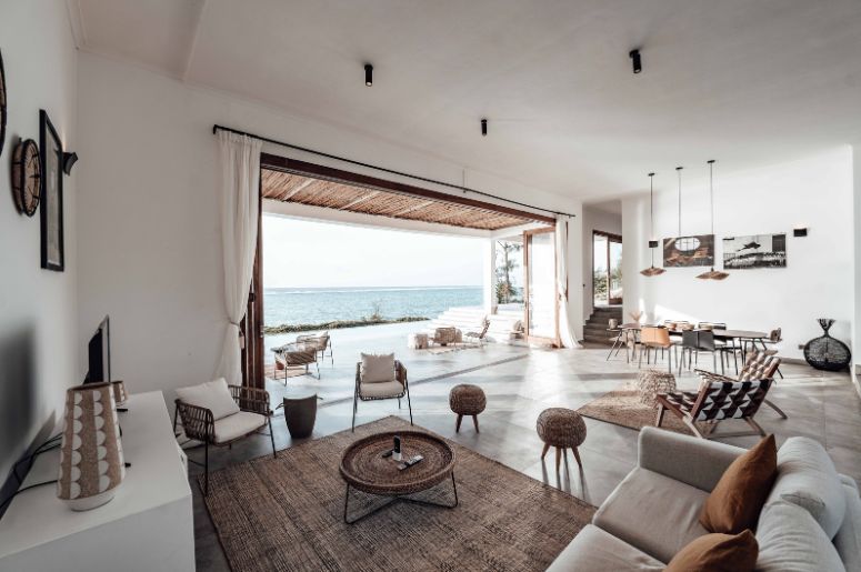 Sala ampla e integrada com sofá, poltronas, mesa de jantar e abertura para área externa com vista para o mar