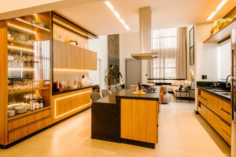 Cozinha integrada à sala de estar, com ilha central, armários de madeira e iluminação decorativa