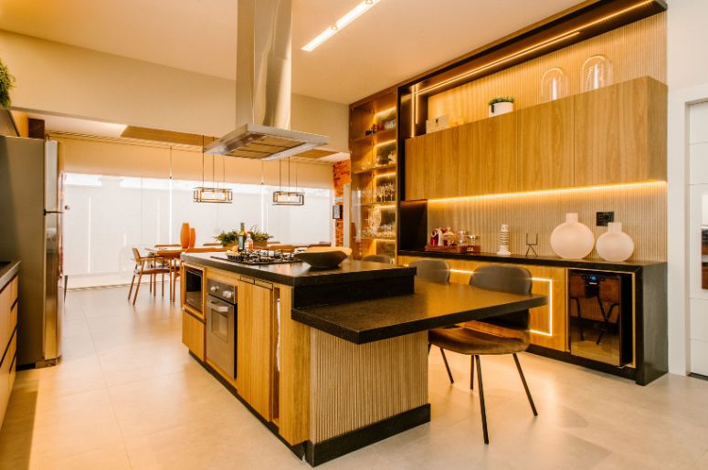 Cozinha planejada com ilha central, armários de madeira, bancada preta e iluminação embutida