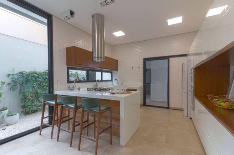 Cozinha moderna com península branca, banquetas de madeira, armários planejados e ampla entrada de luz natural