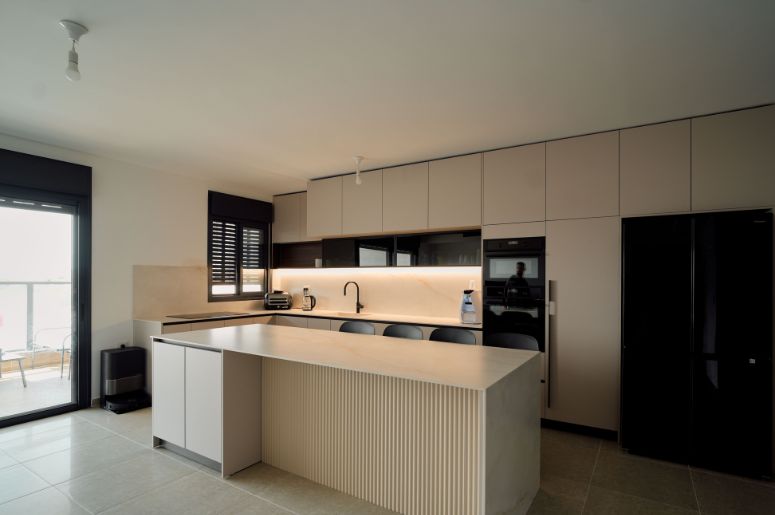Cozinha planejada moderna com ilha central, armários claros, eletrodomésticos embutidos e bancada para refeições
