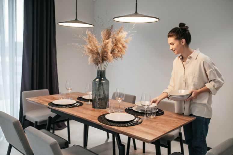 Mulher organizando pratos sobre mesa de jantar de madeira posta para uma refeição