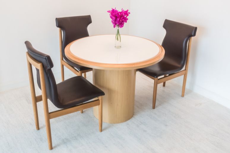Mesa de jantar redonda com três cadeiras estofadas e vaso com flores ao centro
