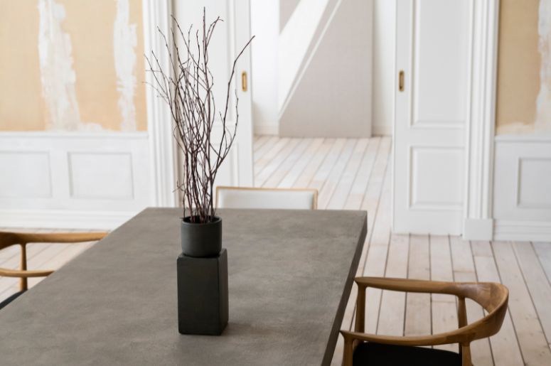 Mesa de jantar retangular em ambiente claro, acompanhada de cadeiras de madeira e vaso decorativo
