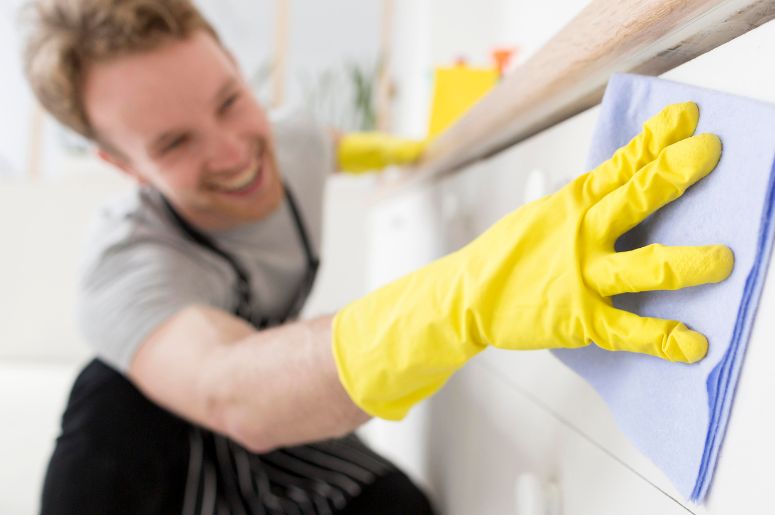 Homem limpando a superfície de um móvel branco com pano e luvas de proteção