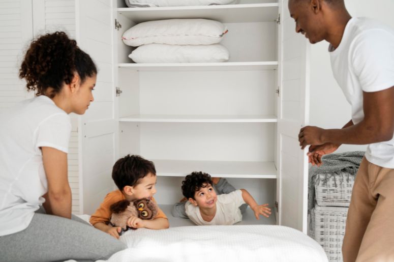 Família organizando um guarda-roupa branco em um quarto, com crianças brincando próximas ao móvel