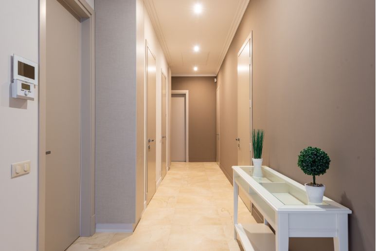 Corredor estreito com aparador branco, plantas decorativas e iluminação embutida no teto