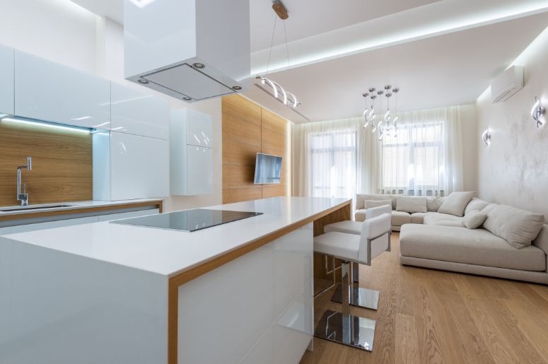 Cozinha e sala integradas com ilha branca, marcenaria em madeira e sofá off-white