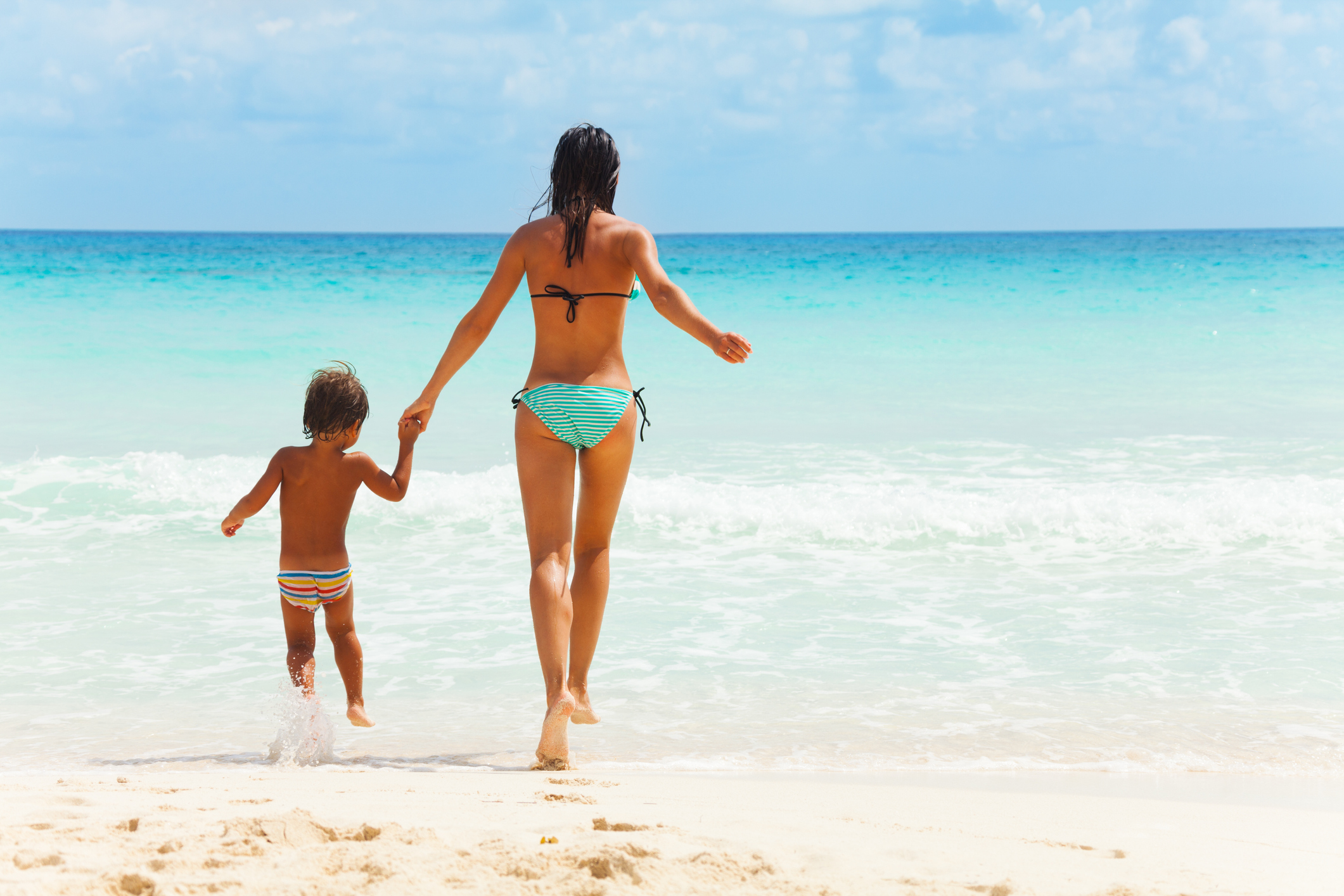 Mother walking into the ocean with her kid