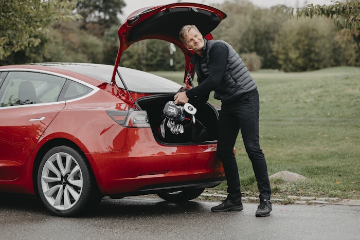 mand med golftaske og tesla