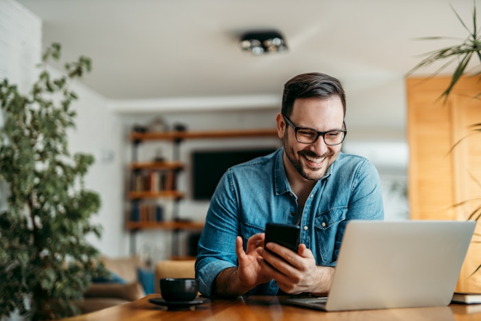 Glad mand ved computer med smartphone