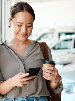 Kvinde med telefon og kaffe hos bilforhandler