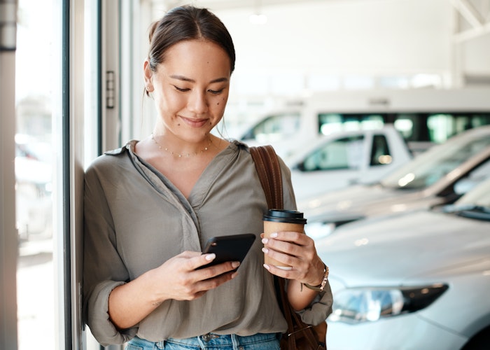 Kvinde med telefon og kaffe hos bilforhandler