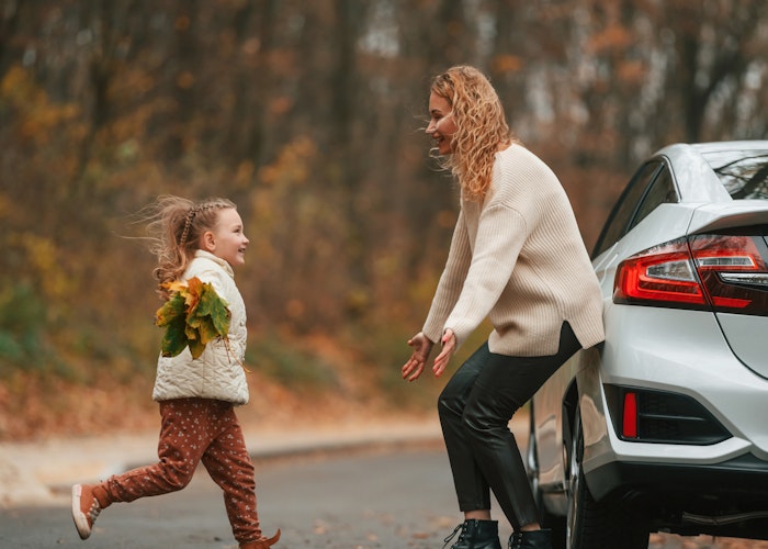 A child runs towards her mother, who stands against a vehicle