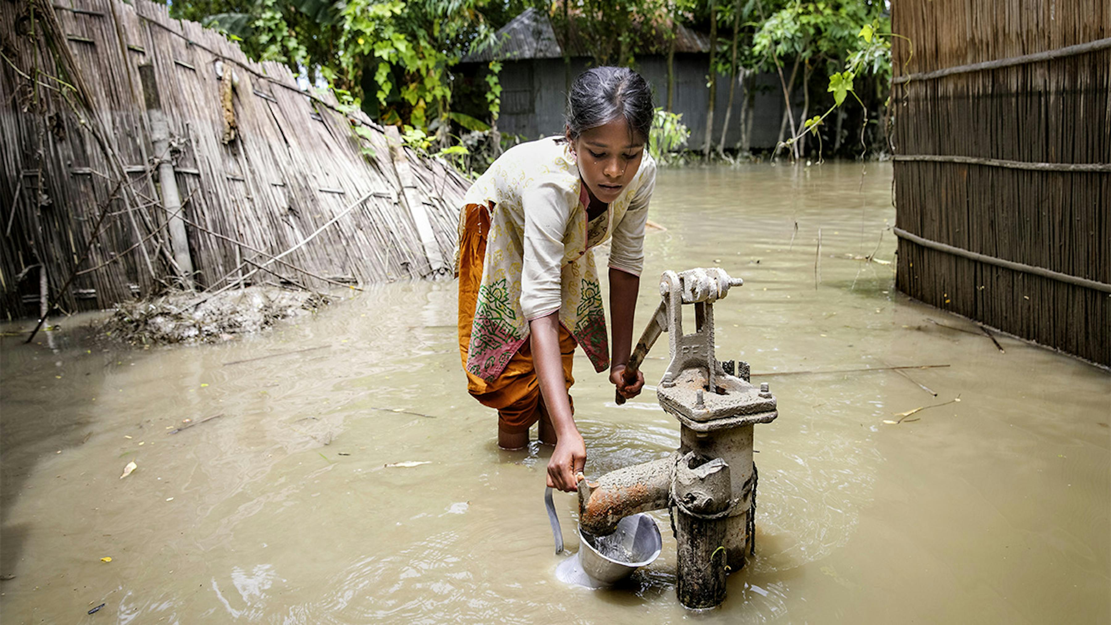 Bangladesh, durante un'inondazione una ragazza cerca di prendere acqua pulita da una pompa.