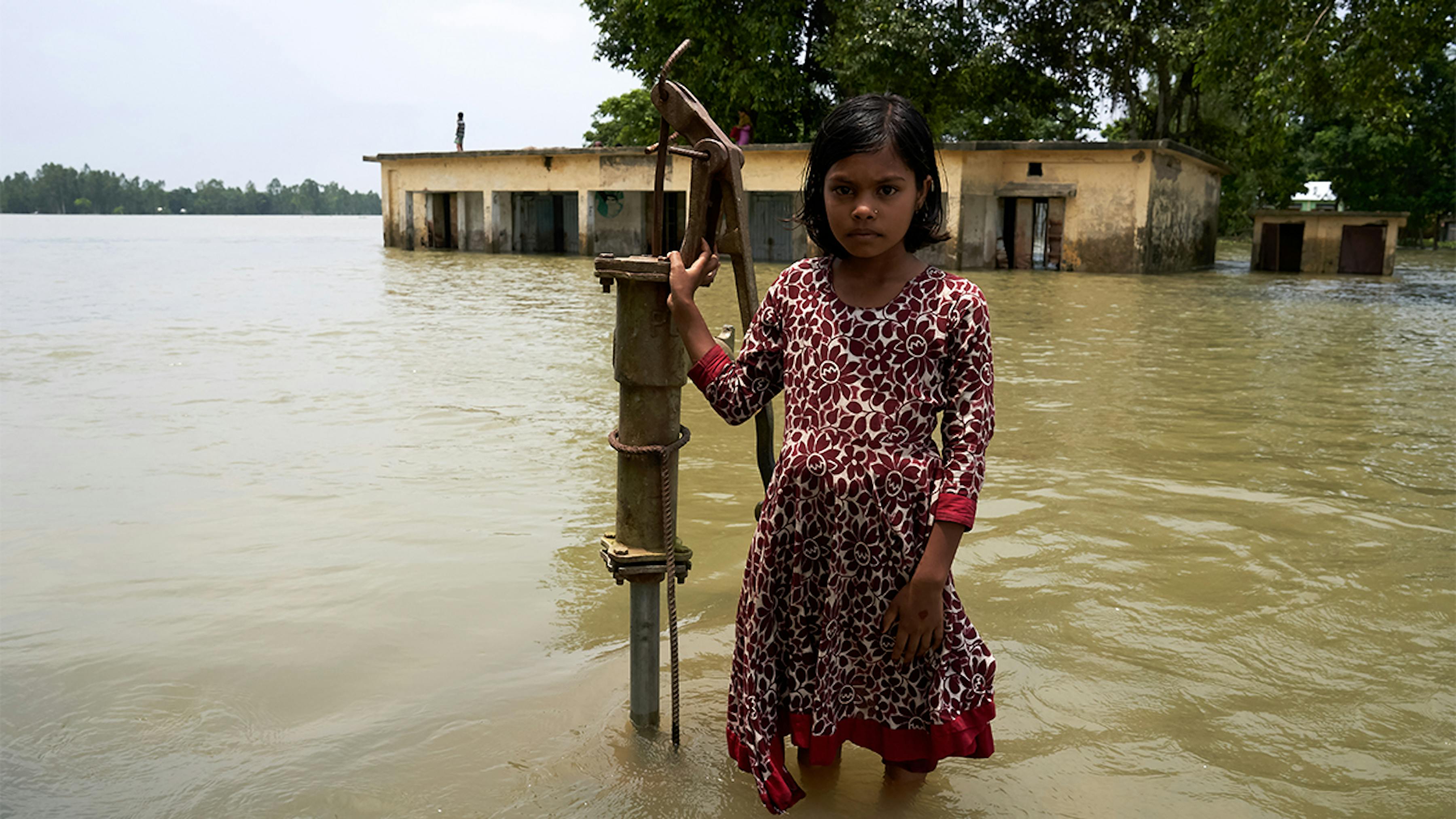 2019, Bangladesh. Una bambina di fronte alla sua scuola parzialmente sommersa dalle acque.