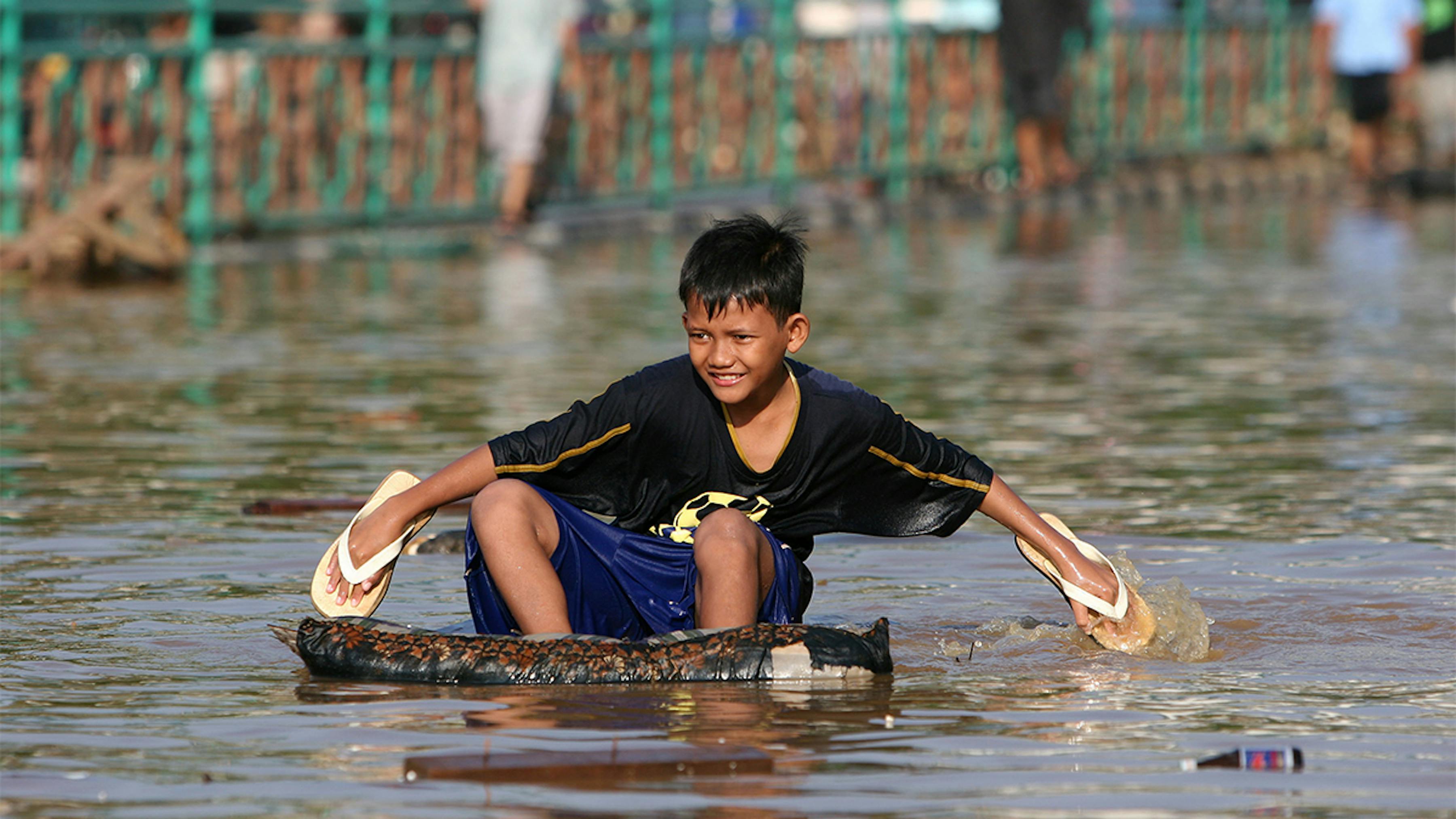 Indonesia, un ragazzo su un galleggiante improvvisato  usa le sue scarpe per remare.