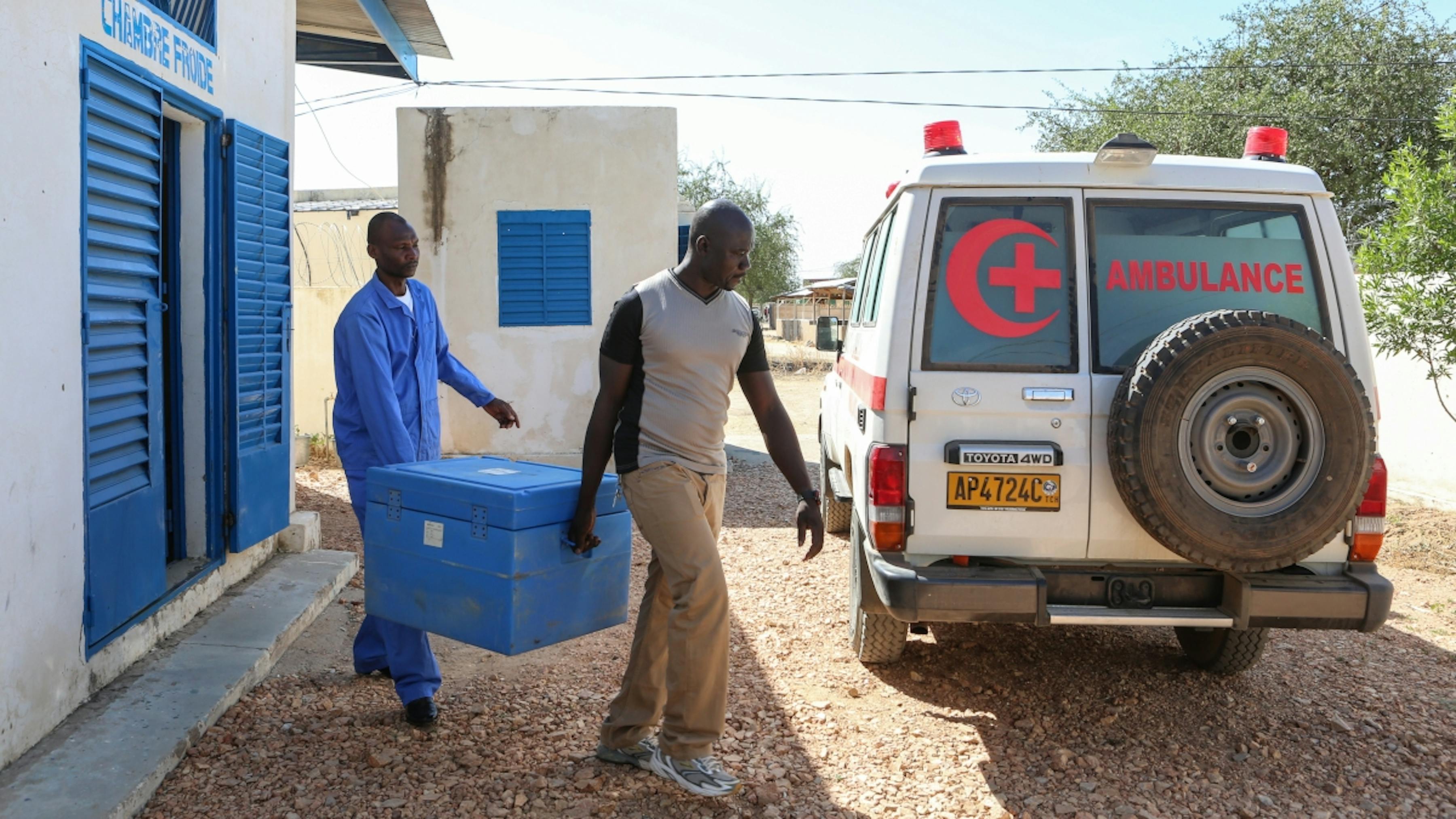 Ciad, due operatori trasportano un contenitore frigo di vaccini a un'ambulanza della Croce Rossa