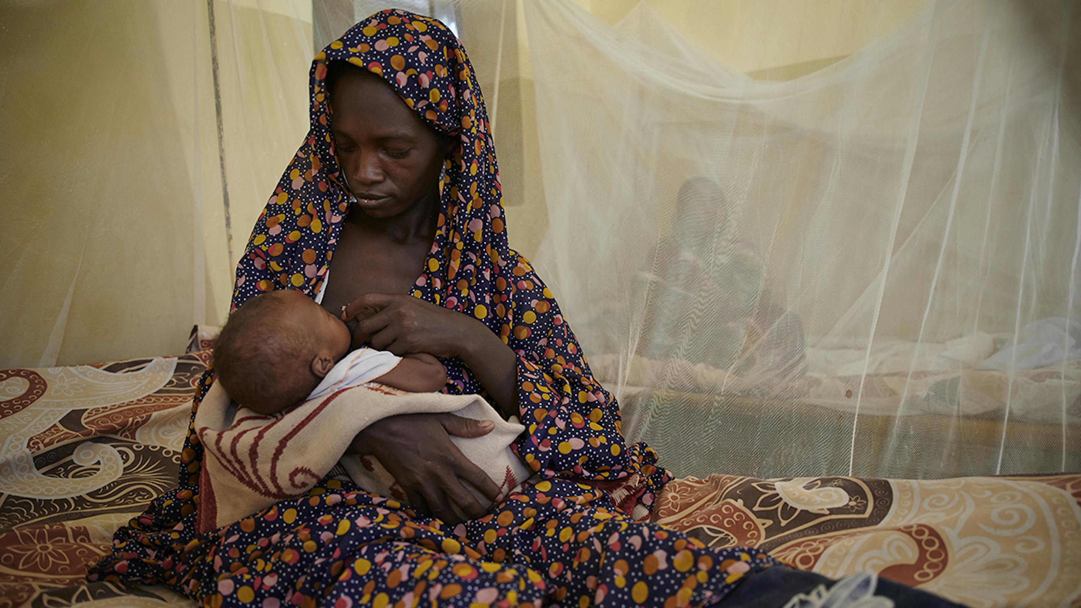 Sudan, seduta su un letto, sotto una zanzariera, una mamma allatta suo figlio al seno