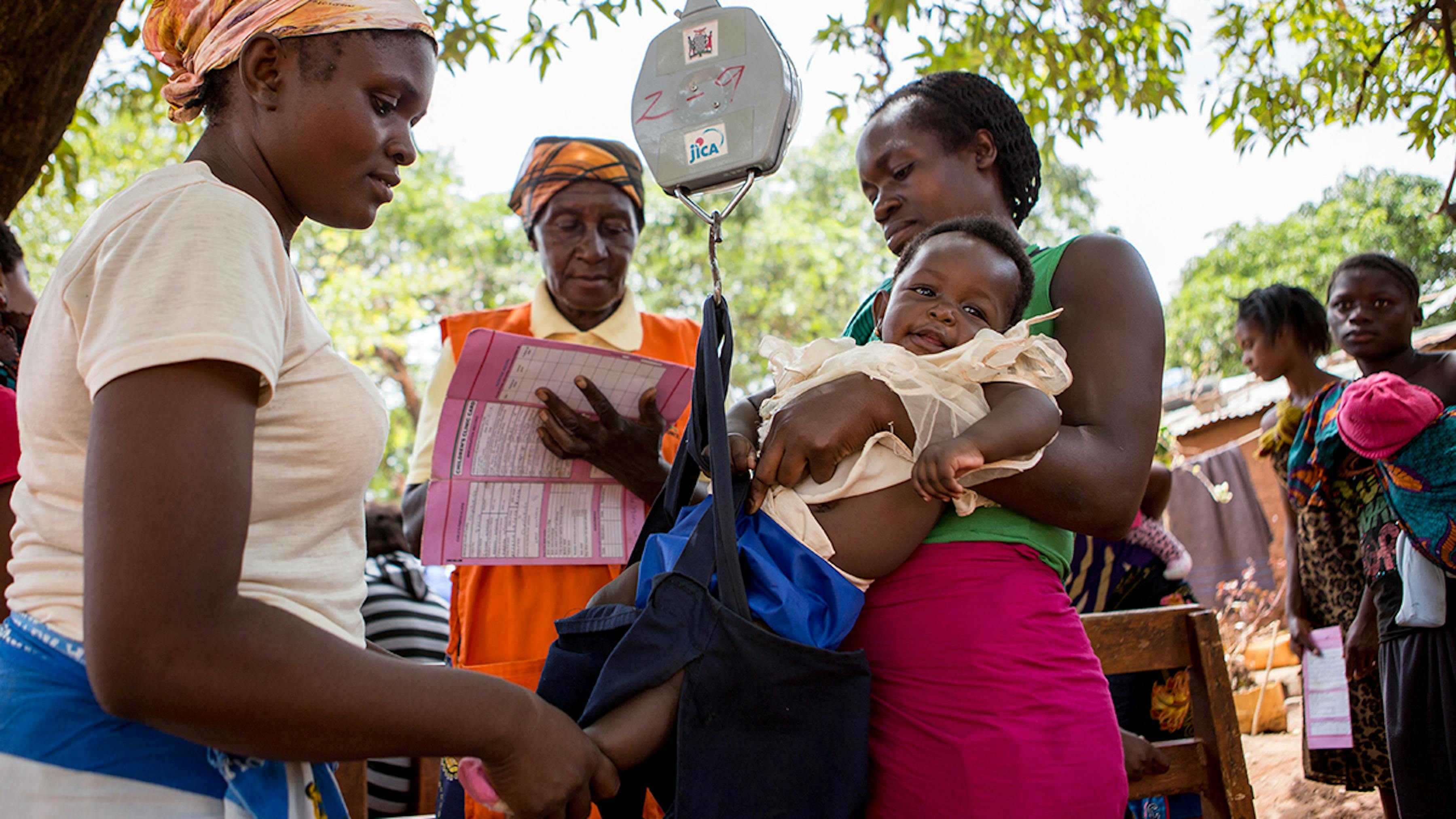 Zambia, un bambino viene pesato da un'operatrice comunitaria mentre la collega prende appunti sul peso