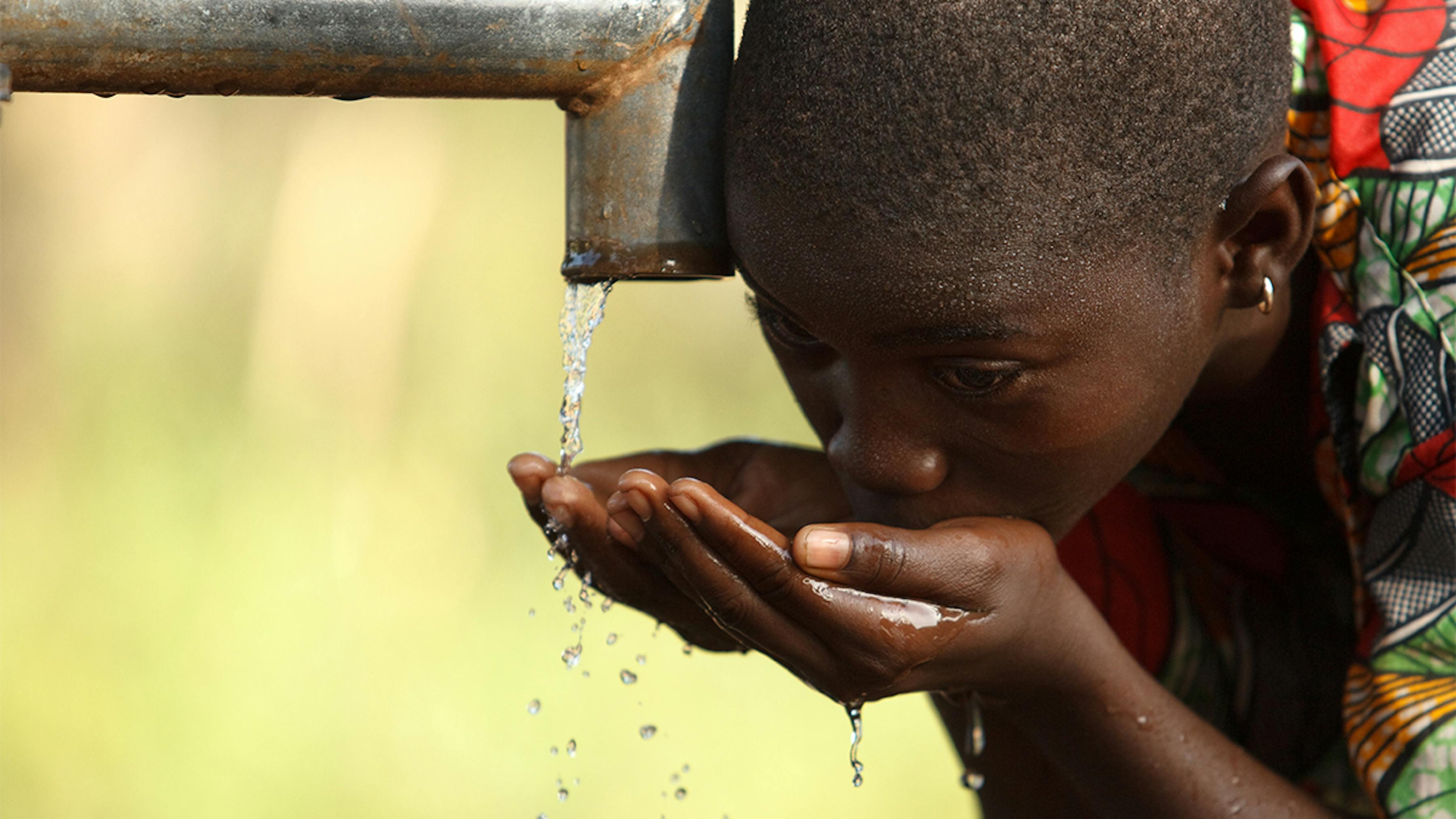 Ghana, una ragazza si disseta da una pompa per acqua a mano nel suo villaggio