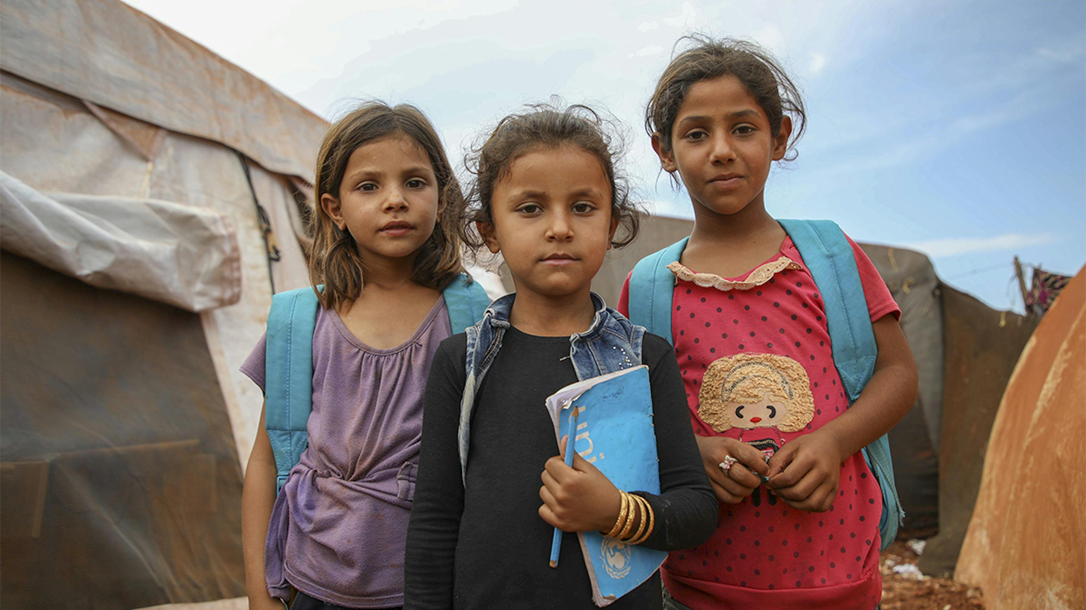 Siria, ragazze con zaini e quaderni UNICEF fuori da una tenda scuola.