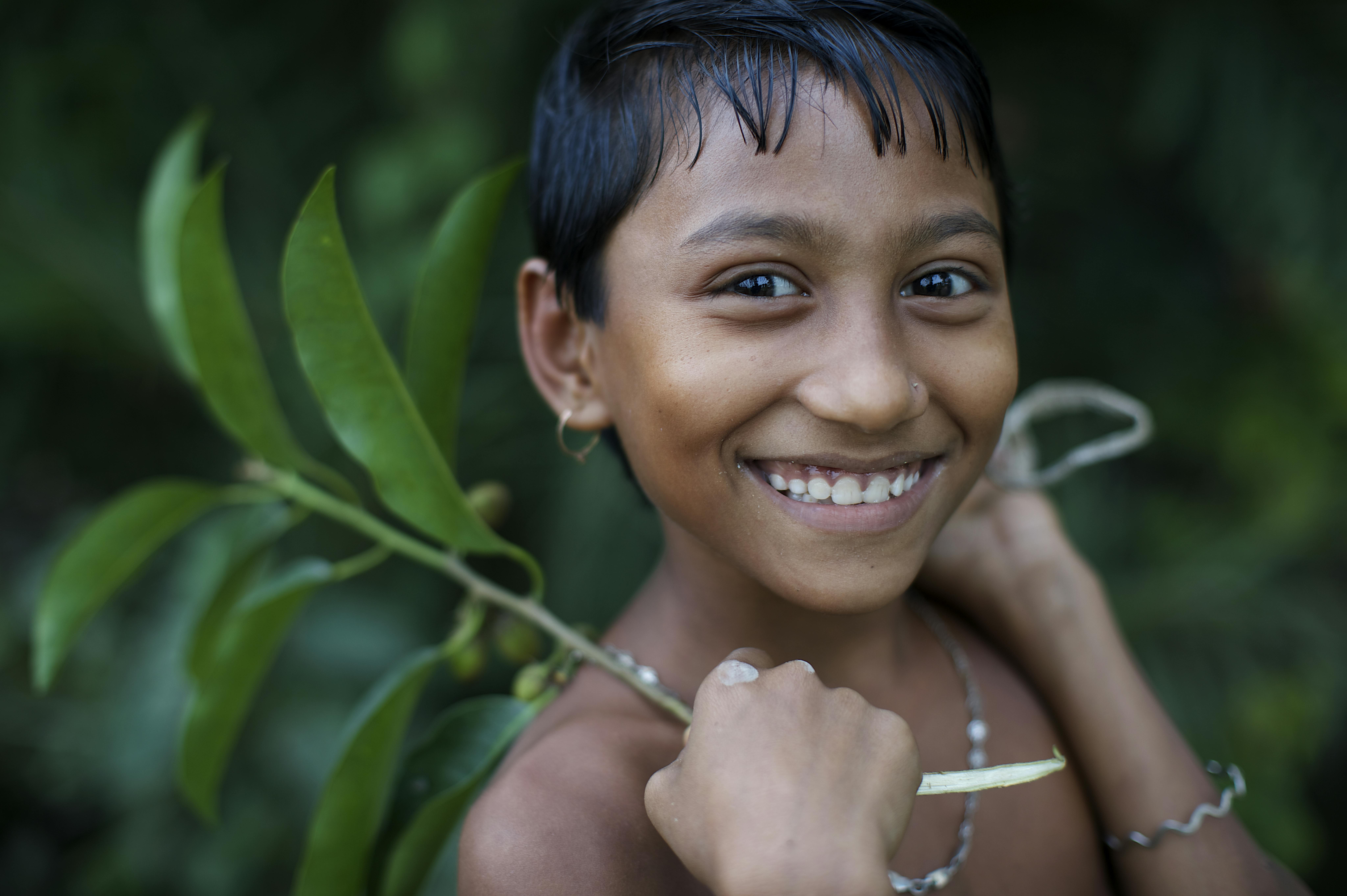 Una bambina con una fronda in mano sorride nel villaggio di Kalaboho, in Bangladesh
