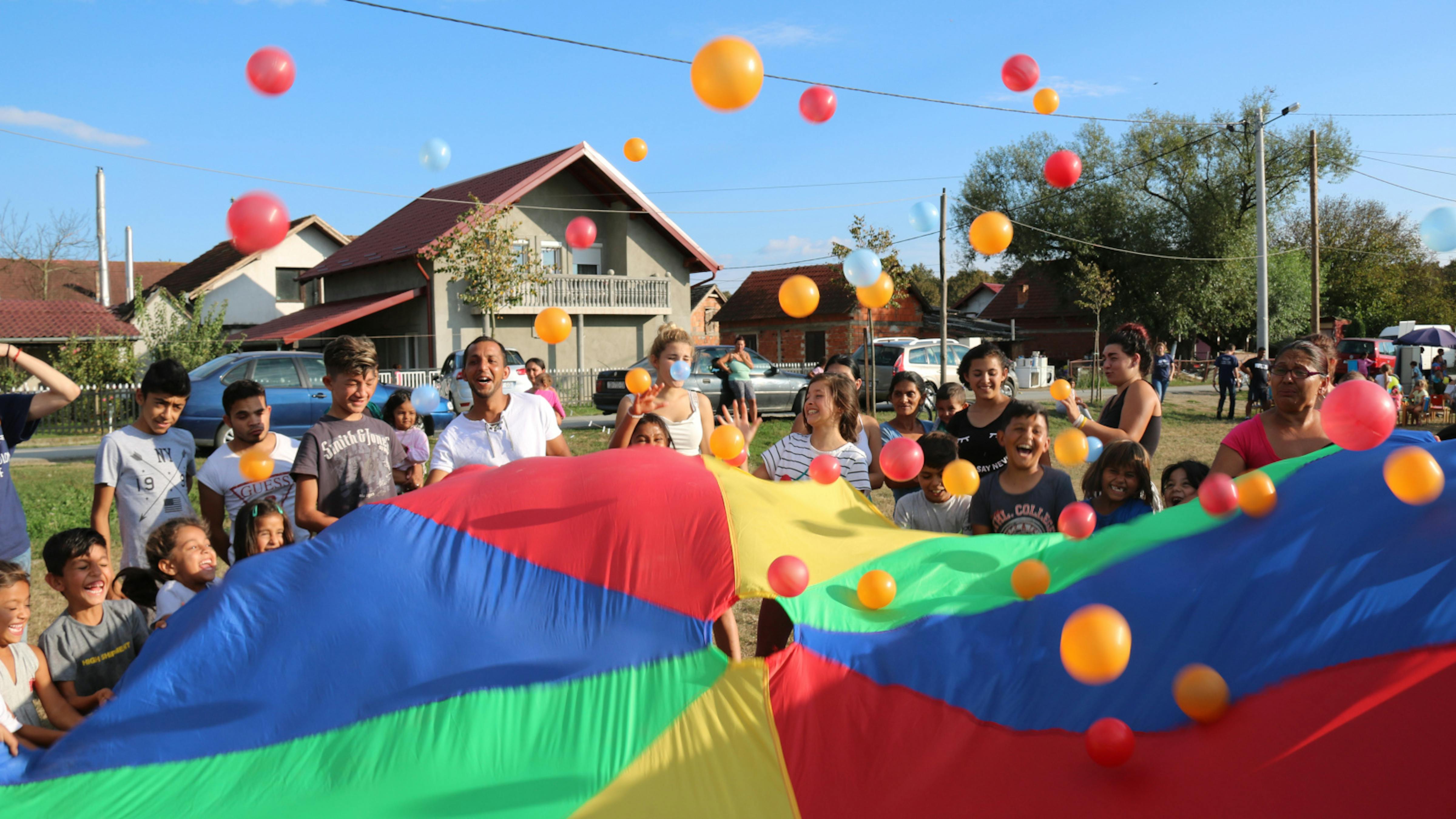 Adulti e bambini giocano con un telo colorato_Utopia