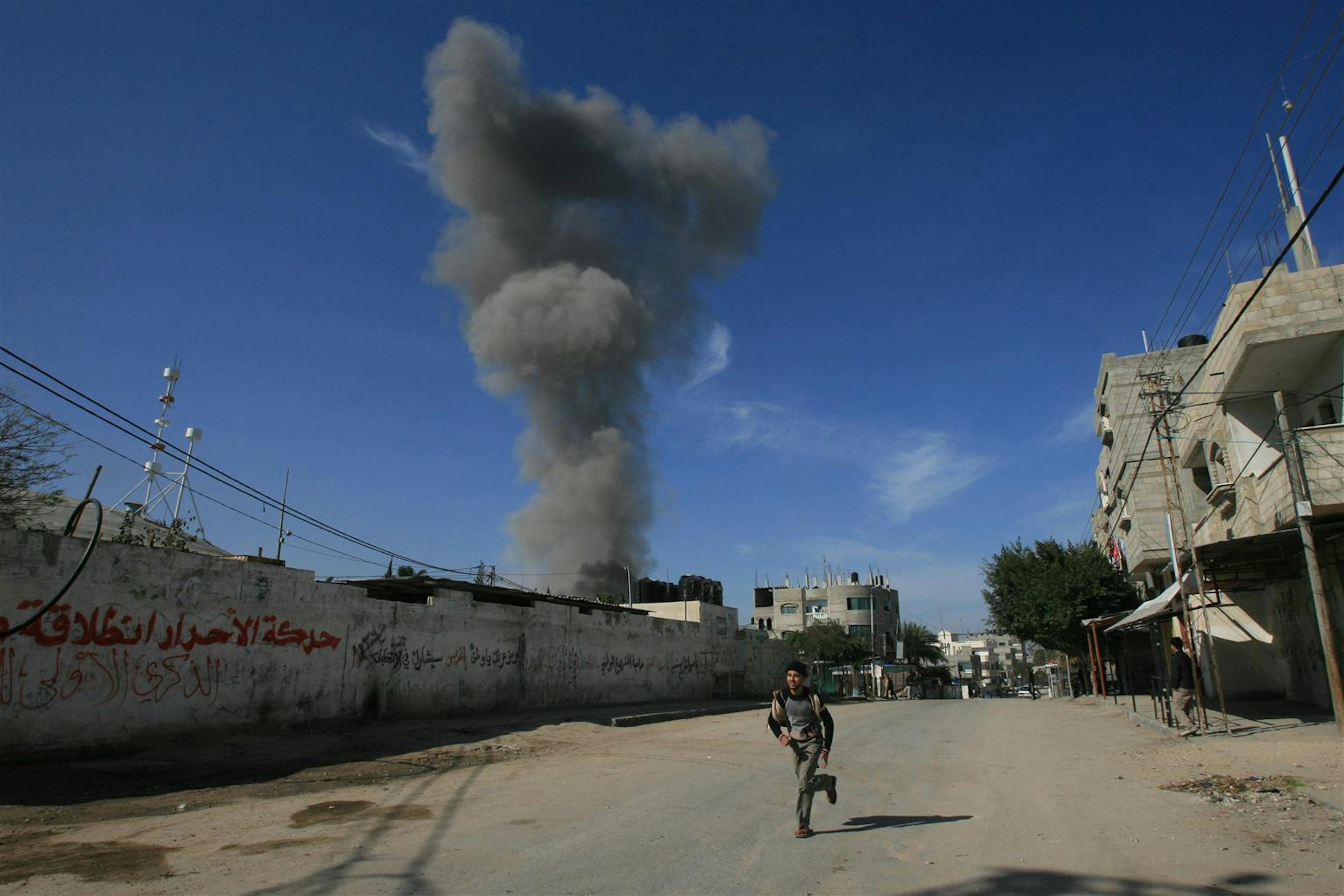 Palestina, un ragazzino scappa lungo una strada nella città meridionale di Rafah. Sullo sfondo, il fumo sale dai serbatoi di carburante colpiti durante l'incursione militare in corso