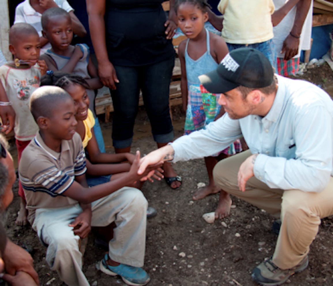 Robbie Williams parla con Denise, 9 anni, e suo fratello, che vivono in una tendopoli a Jacmel (Haiti). Denise è tornata a scuola grazie all'UNICEF - ©Simon Niblett/UNICEF/2010