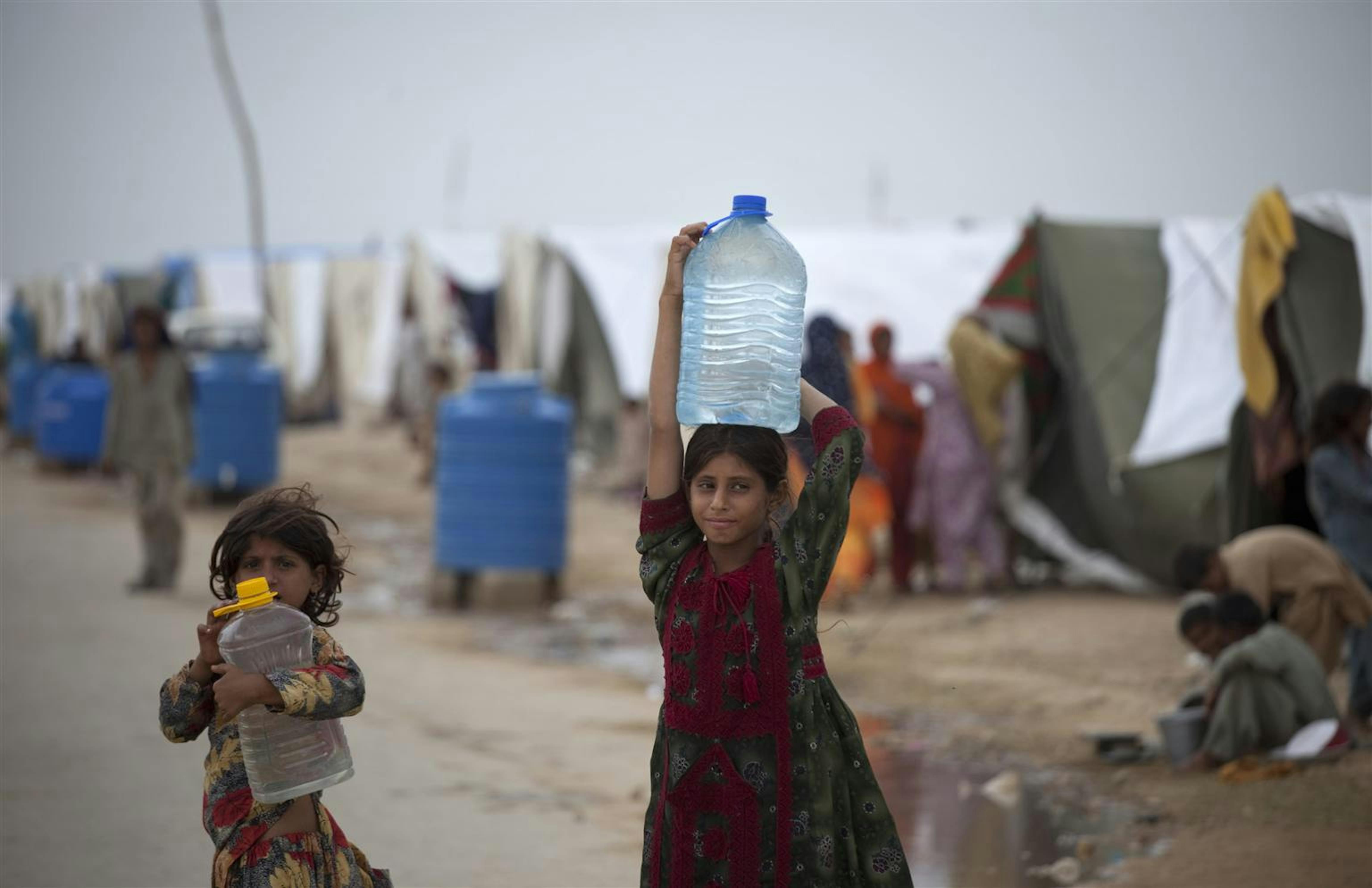 Due bambine trasportano acqua potabile in un campo per sfollati di Karachi (Pakistan): sullo sfondo, alcuni serbatoi idrici installati dall'UNICEF - ©UNICEF Pakistan/2010-275/M.Ramoneda