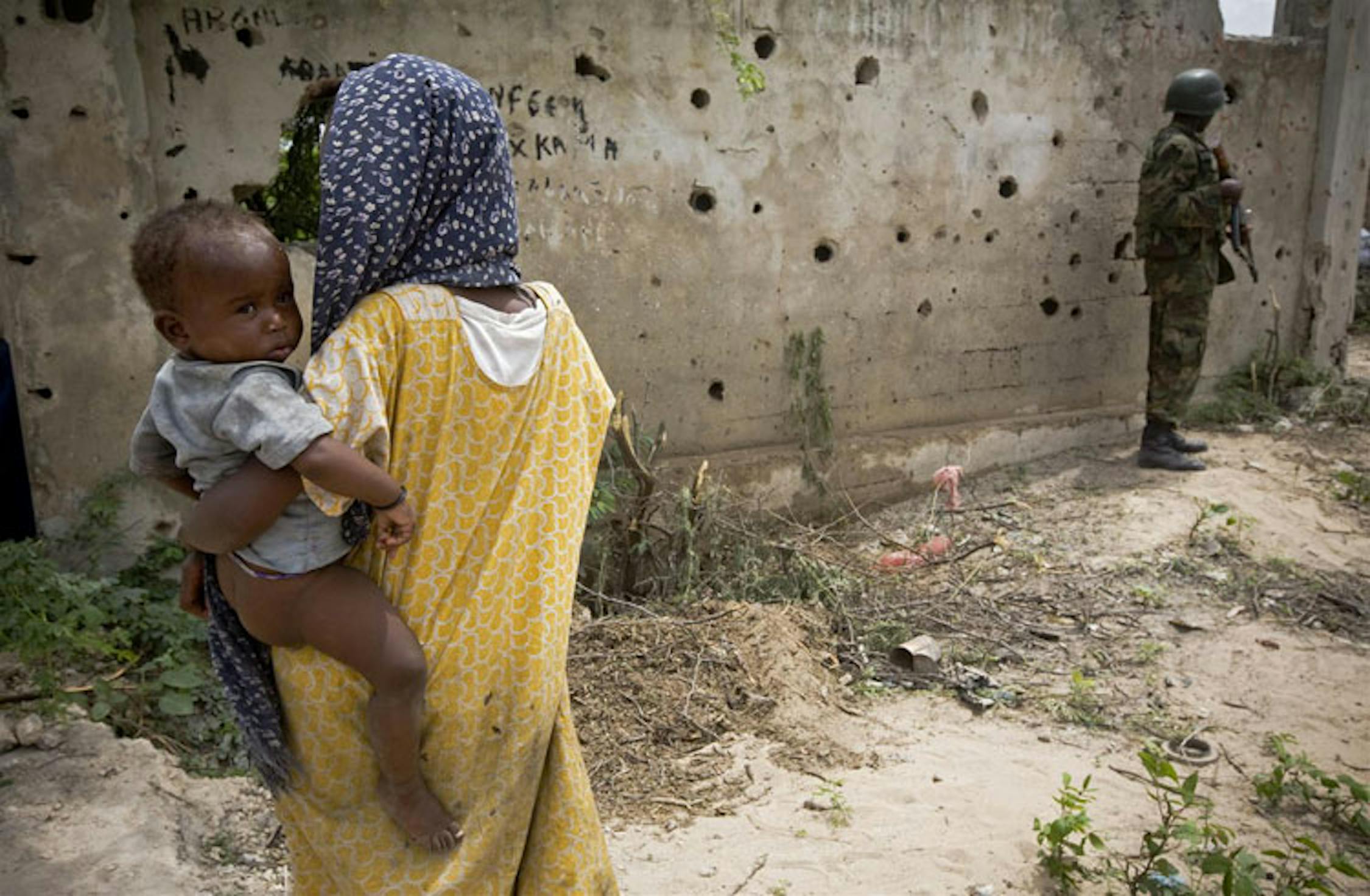 Un muro crivellato dai proiettili, un uomo armato, desolazione intorno: il panorama abituale di un campo per sfollati a Mogadiscio, Somalia - ©UNICEF/NYHQ2011-1194/K.Holt